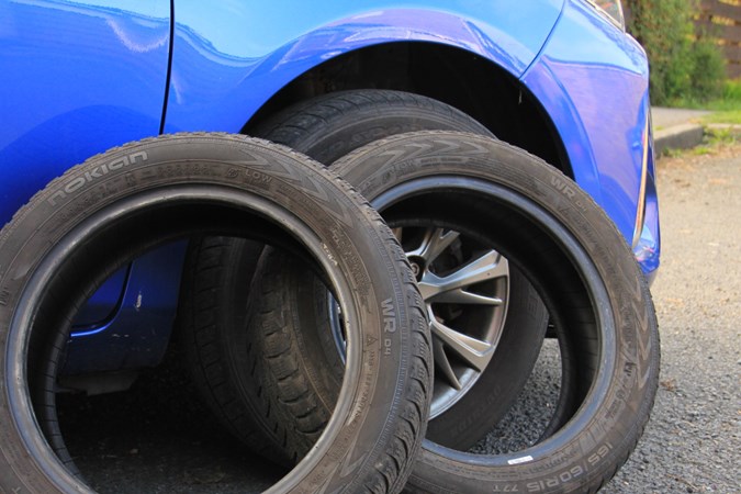 Part-worn tyres propped up against the wheel arch of a blue car