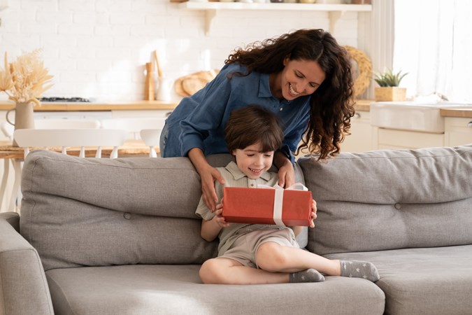Mother giving a little boy sitting on a sofa a gift