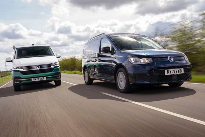 Two campervans, a blue VW Caddy and a green and white VW California drive side by side on a road 