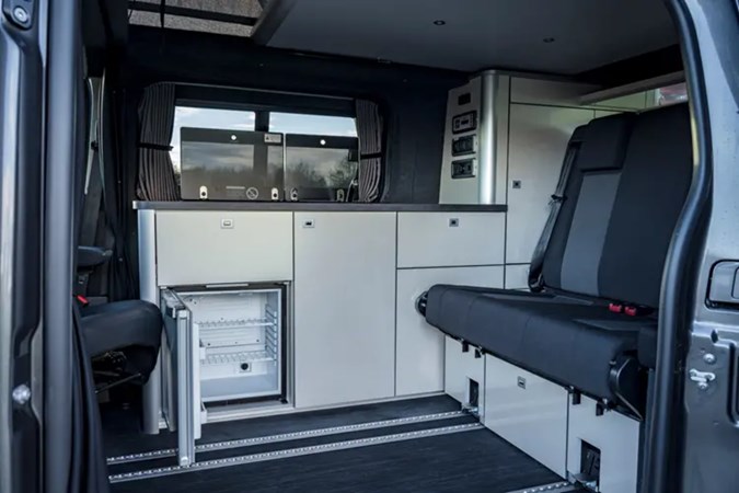 Interior of the Vauxhall Vivaro campervan showing bench seats, kitchen units and fridge with open door