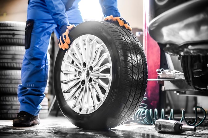 Technician with orange gloves holds up a tyre with gleaming wheels, next to tyre fitting equipment