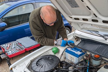 Bonnet open with battery in clear view, tools laid out on the wing or scuttle panel Alt text: Open bonnet with car battery visible and tools ready for replacement - how to change a car battery