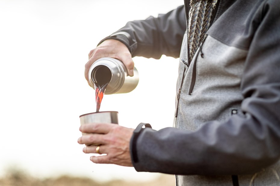 Person using a thermal flask to pour a cup of coffee outdoors