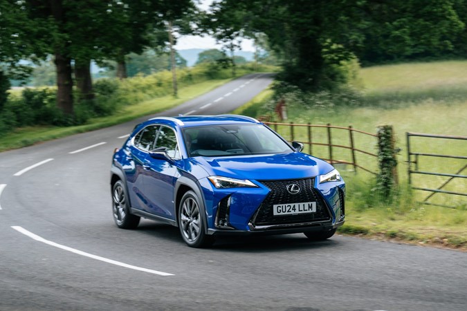 A blue Lexus UX compact SUV seen from the front three quarters driving around a bend in a country road