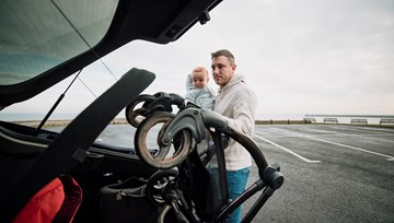 Man holding baby, pushchair going into a car