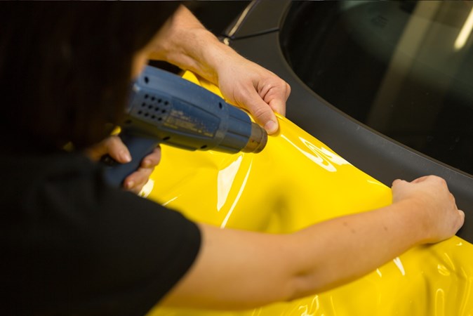 Yellow wrap being applied by heat to a car panel
