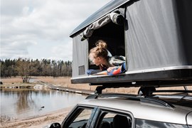 A person looking out of a car tent at some water