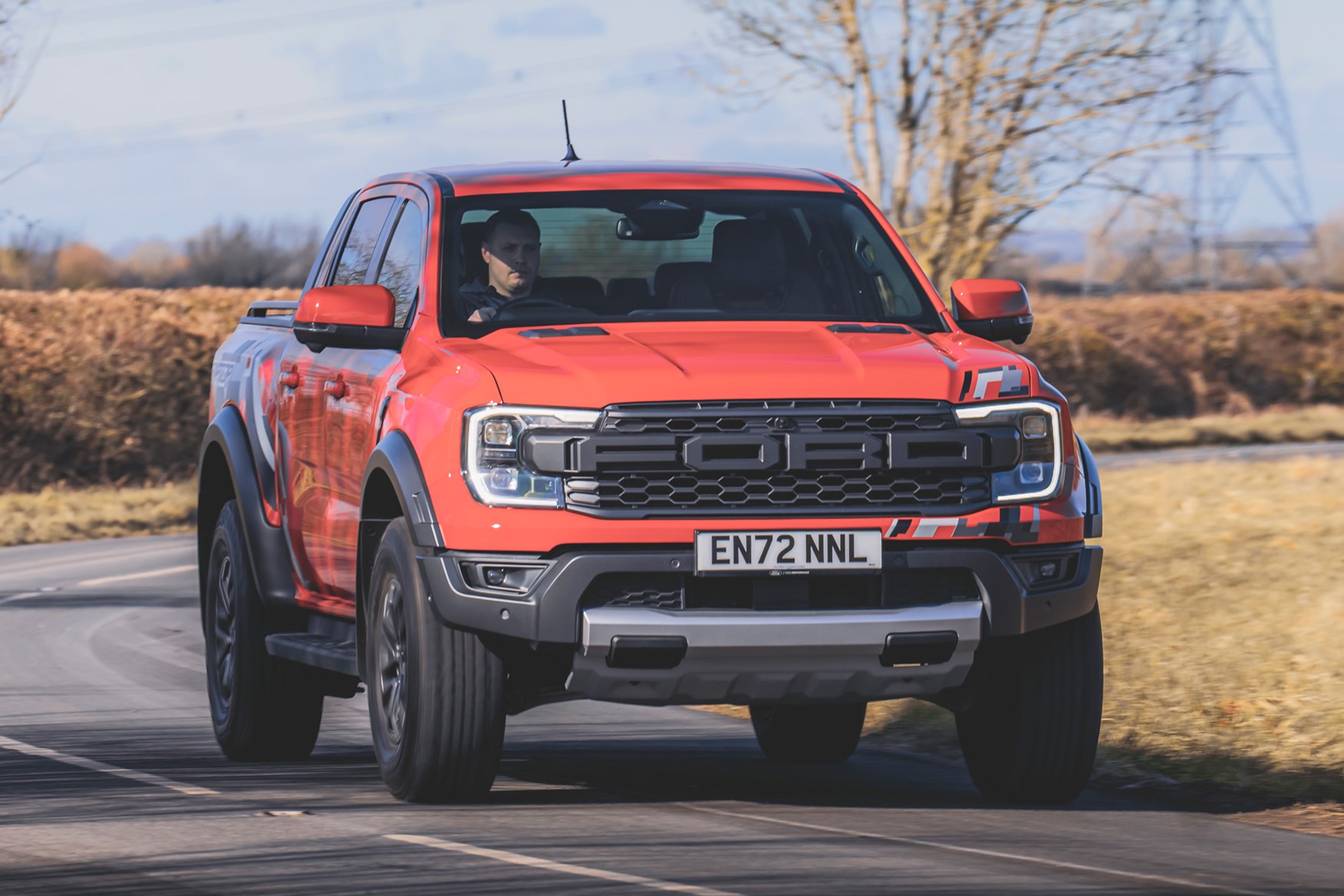Ford Ranger Raptor (2023) review: front cornering shot on exit, orange paint, country road