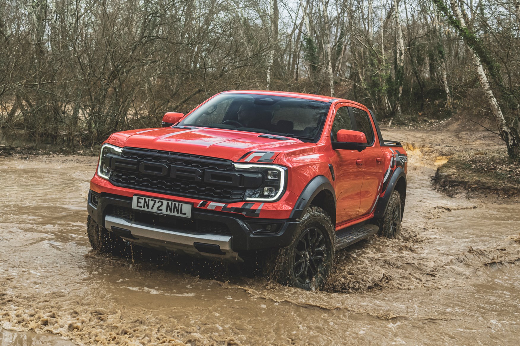 Ford Ranger Raptor (2023) review: wading through water, front three quarter, orange paint, forest trail