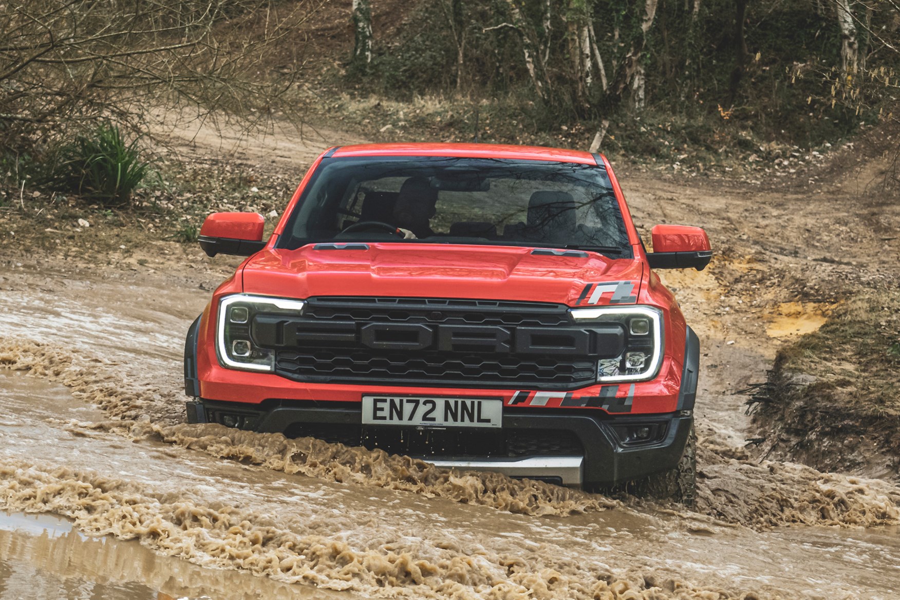 Ford Ranger Raptor (2023) review: wading through water, front head-on, orange paint, forest trail