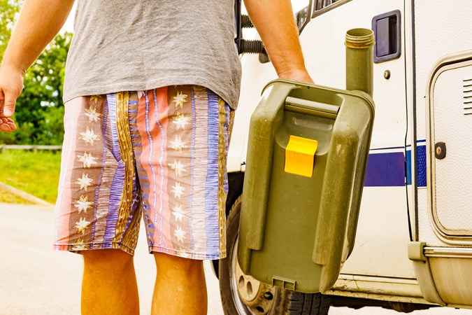 Man in shorts carries a toilet cassette from a caravan