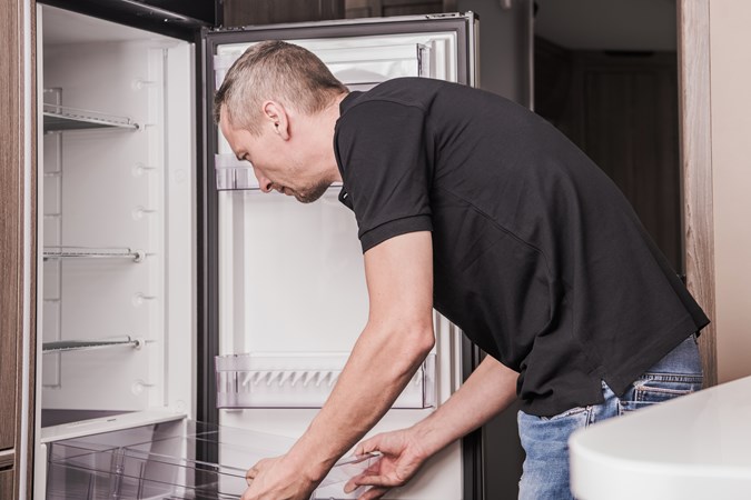 A man handles the salad drawer of the caravan fridge