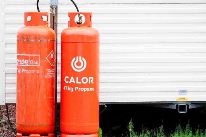 A close up of two orange Calor gas cylinders connected to a static caravan