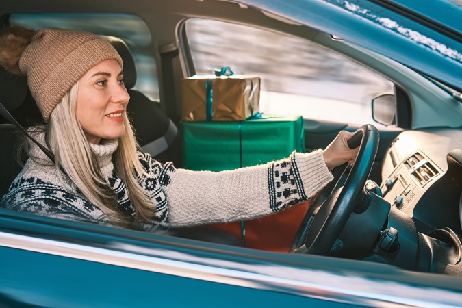 Blonde woman in wool hat sits at wheel with Christmas presents on passenger seat