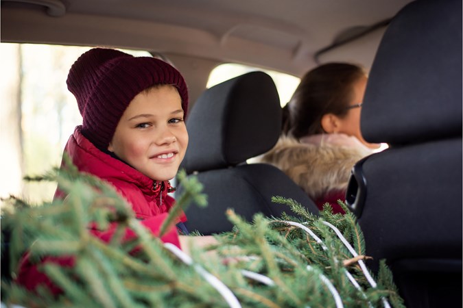 Child looks back to camera from rear seat, woman sits in passenger seat, xmas tree can be seen in foreground