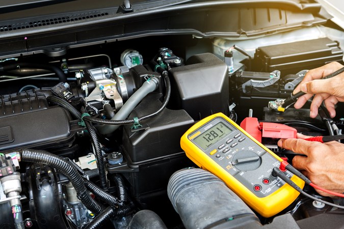 Mechanic testing car battery voltage level with a multimeter