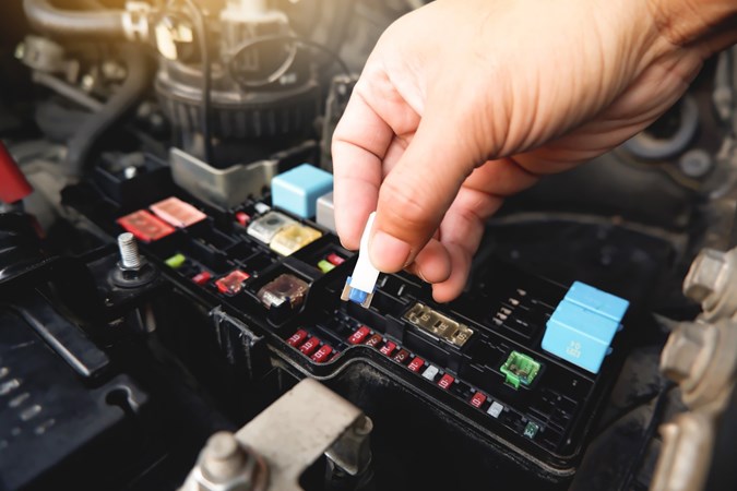 Image of a man's hand removing fuse from a car fuse box