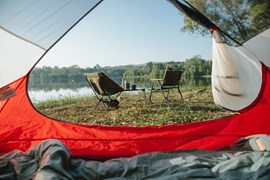 Looking out of a tent door onto two camping chairs and a lake