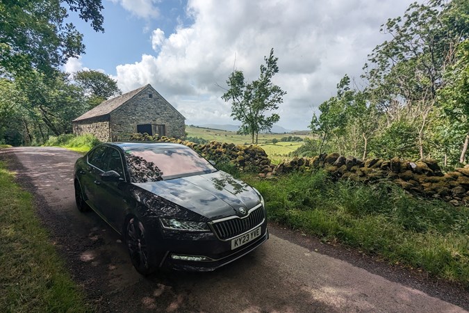 Skoda Superb long termer front three quarter, parked on a Cumbrian B-road, shaded by trees, black paint