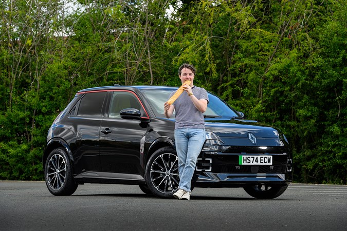 Ryan Gilmore poses with the Renault 5 E-Tech, black paint, exterior, front three-quarters, Ryan holds a baguette