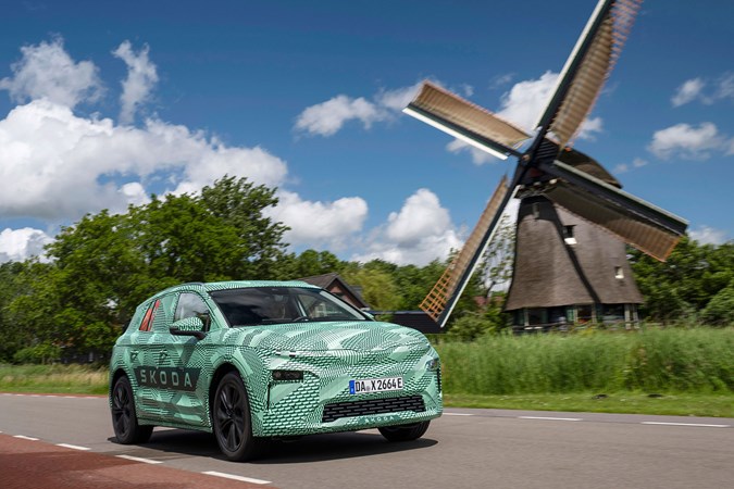 Skoda Elroq prototype: front three quarter driving, windmill in background, green camo wrap