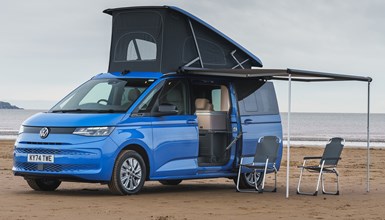 Image of a blue Volkswagen California at the beach with its pop-top up | Parkers cars