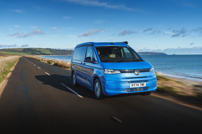 Image of a blue Volkswagen California driving along a country road, viewed from the front right corner