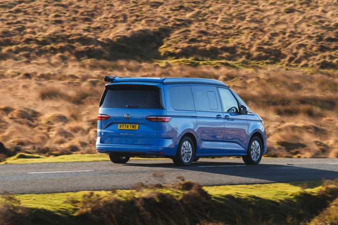 Image of a blue Volkswagen California driving along a country road, viewed from the rear right corner