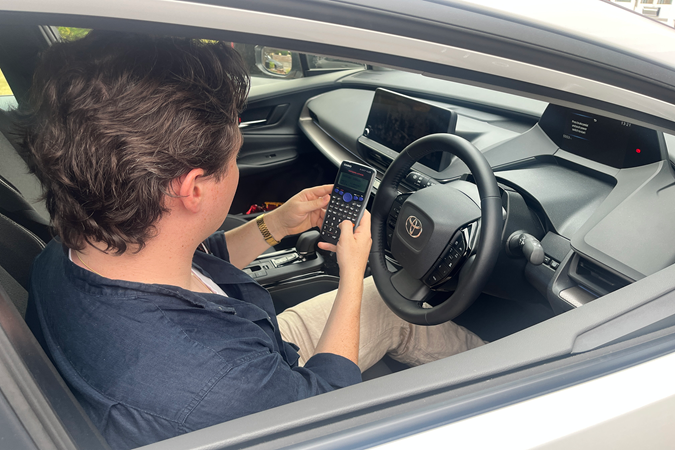 Ryan Gilmore uses a calculator behind the wheel of the Toyota Prius