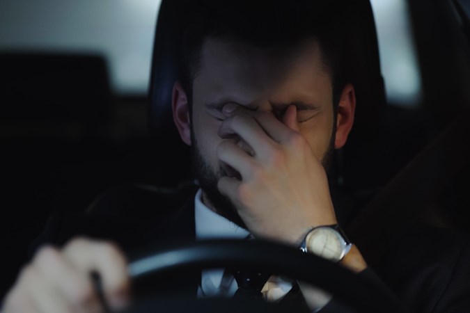 Image of a tired man rubbing his eyes while driving