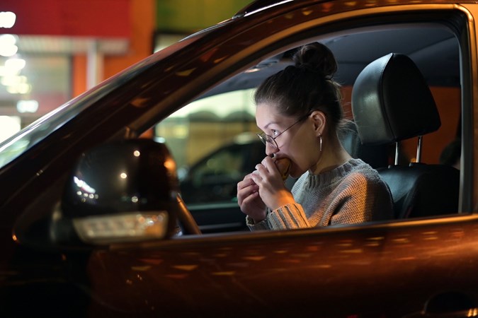 Image of a woman eating while in the drivers seat of a car