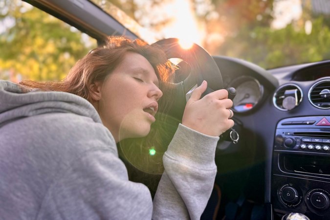 Image of a woman sleeping at the wheel of a car