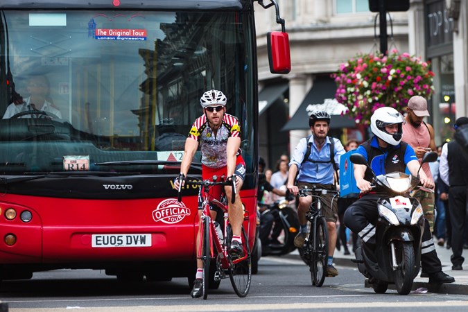 Image of cyclists waiting at traffic lights near a bus