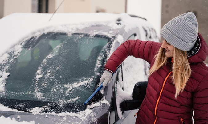 Image of a woman clearing snow off a car