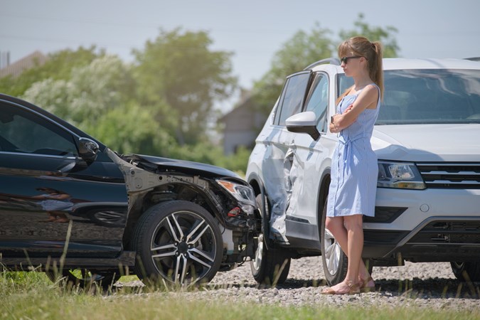 Image of a young woman standing between two crashed cars