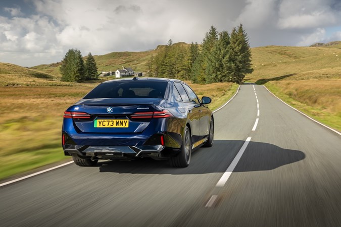 Image of a dark blue BMW i5 driving along a country road, viewed from the rear