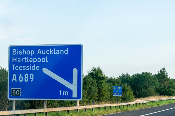 Image of a blue UK motorway road sign directing towards Bishop Auckland