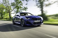 Image of a blue BMW 2 Series driving along a country road, viewed from the front right three-quarters