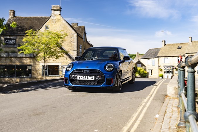 Image of a blue MINI JCW hatchback driving over a bridge, viewed from the front