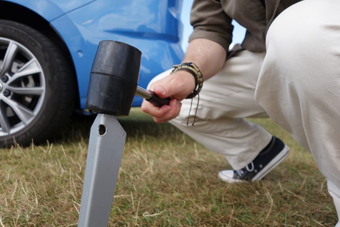 Close-up image of a man hammering guy rope pegs into the ground