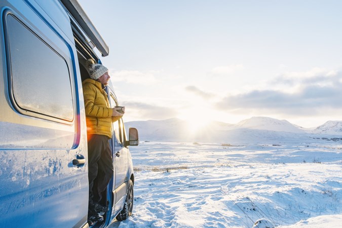 Image of man standing in the doorway of a campervan pitched in a snowy landscape