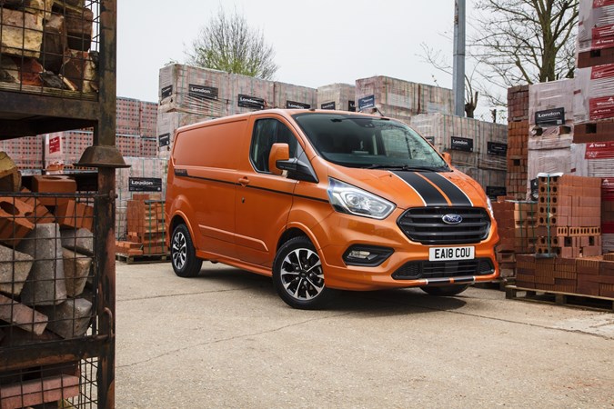 Image of an orange Ford Transit Custom, static in a builders merchant yard, viewed from the front right corner