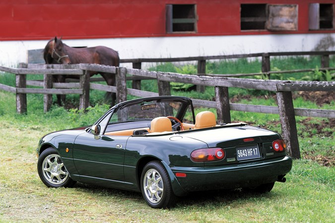 Image of a green JDM Mazda MX-5 in a horse pasture, viewed from the rear left corner