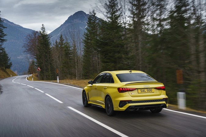 Image of a yellow Audi RS3 driving through a mountain range, viewed from the rear left corner