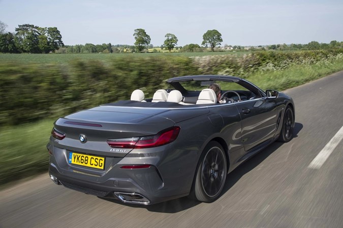 Image of a grey BMW 840d convertible with roof down, viewed while driving from the rear right corner