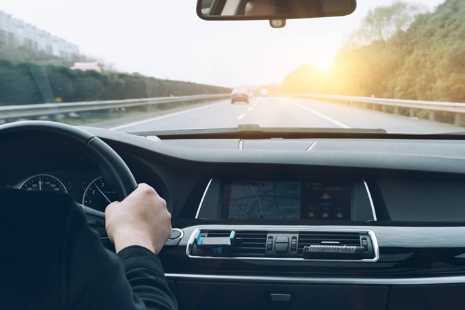 Image of a man driving a BMW along a motorway into the sunset, viewed from the back seat